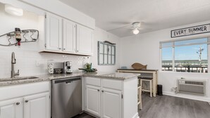 Una cocina moderna con armarios blancos, lavavajillas y una estación para café.