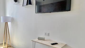 A modern room with a flat-screen TV mounted on the wall, a small wooden table with a remote control, and a floor lamp.