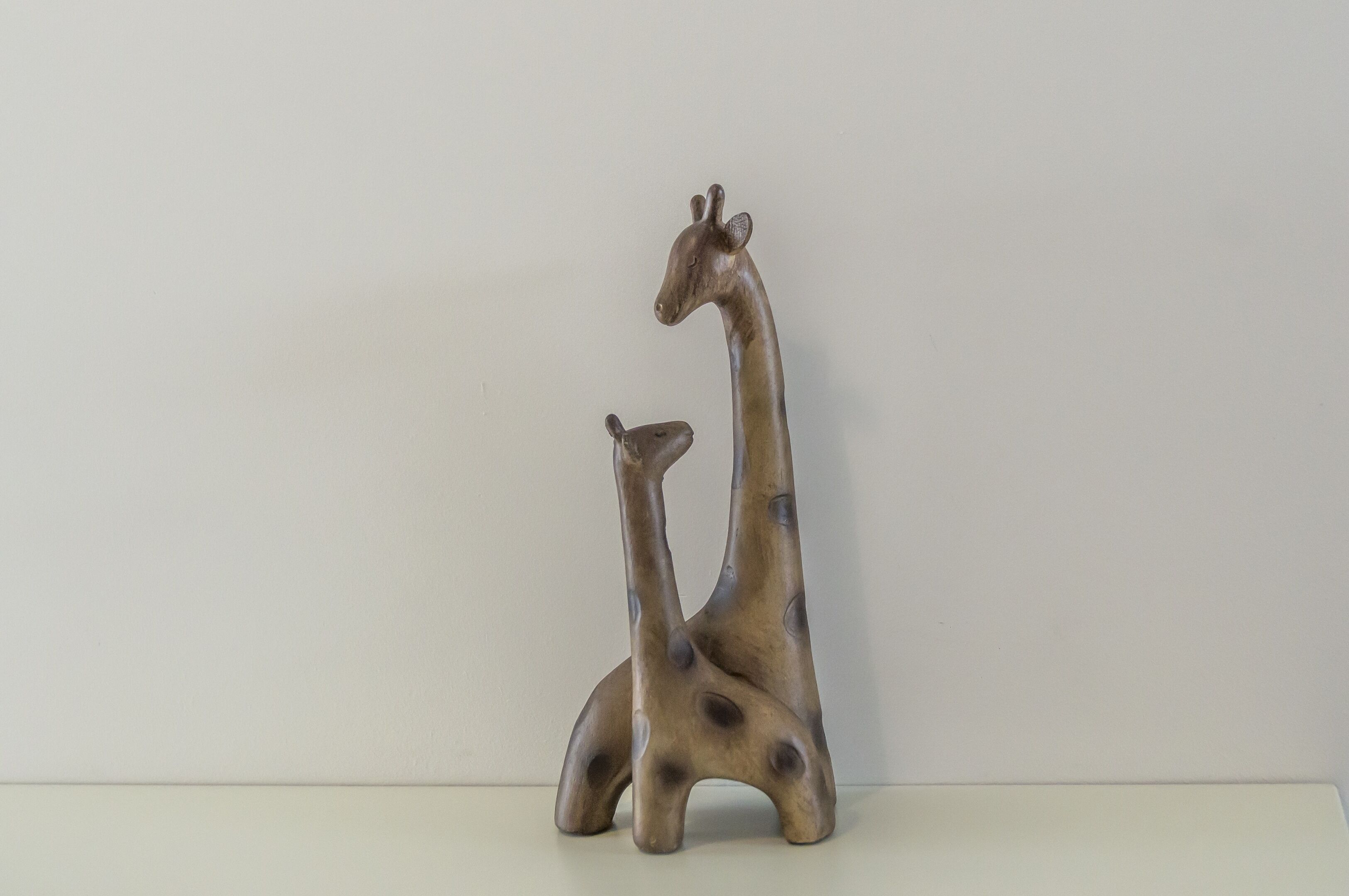 Eine Skulptur von zwei Giraffen, eine größer und eine kleiner, vor einem schlichten Hintergrund.
