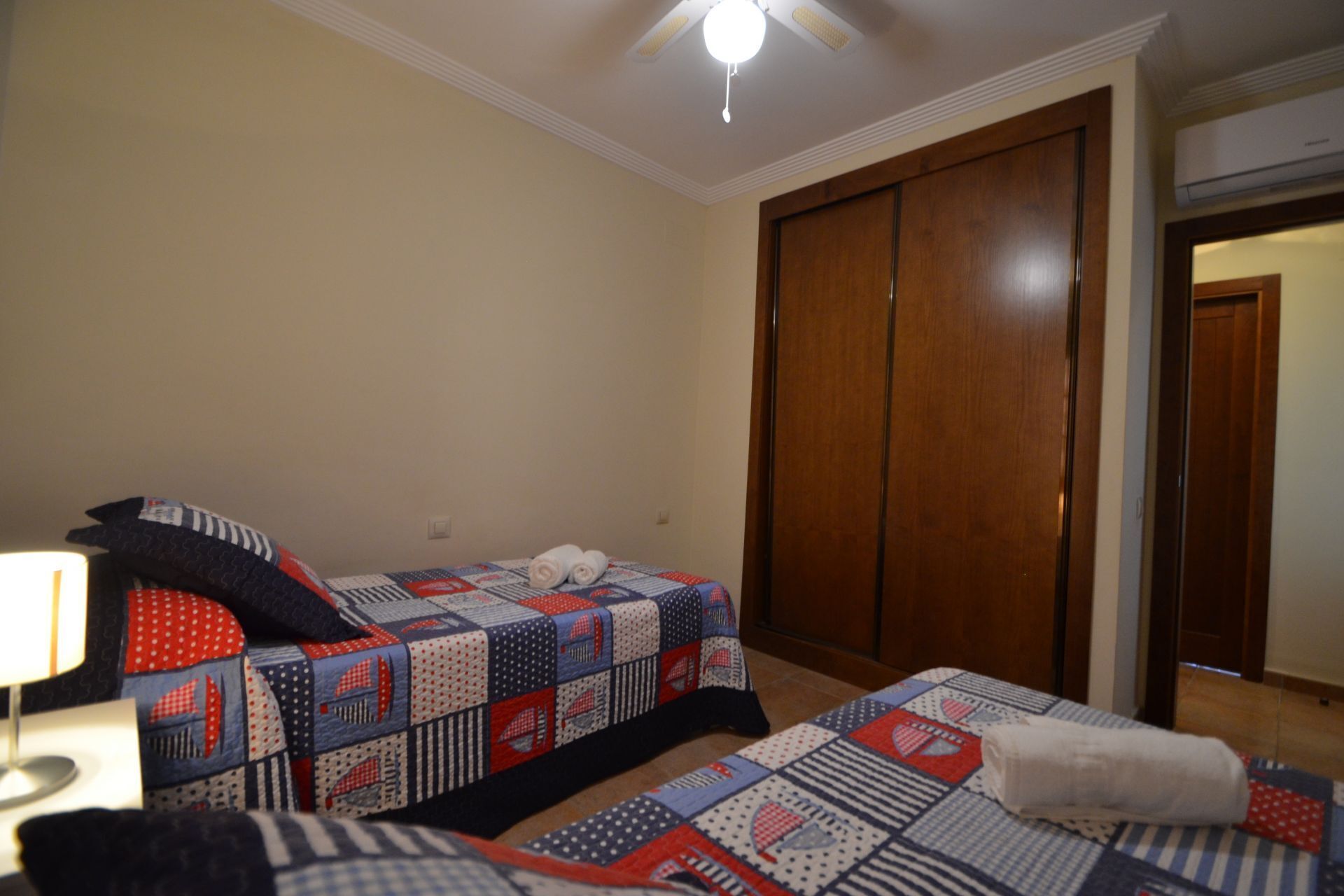 A bedroom with two beds, a wooden wardrobe, and a ceiling fan.