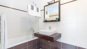Un baño moderno con bañera, un lavabo blanco y un espejo sobre él.