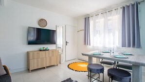 Una cocina moderna con comedor, un televisor en la pared y una puerta que da a otra habitación.