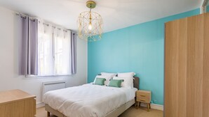 Un dormitorio con cama, mesita de noche, cómoda y ventana con cortinas.