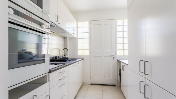 Una cocina moderna con armarios blancos, horno empotrado y una ventana con persianas.