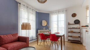 A living room with a red sofa, a dining table with red chairs, a wooden coffee table, and a bookshelf.