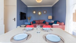 A dining area with a table set for two, a sofa, and a television mounted on the wall.
