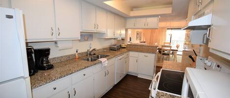 A compact kitchen with white cabinets, a granite countertop, a built-in stove, and a coffee maker.