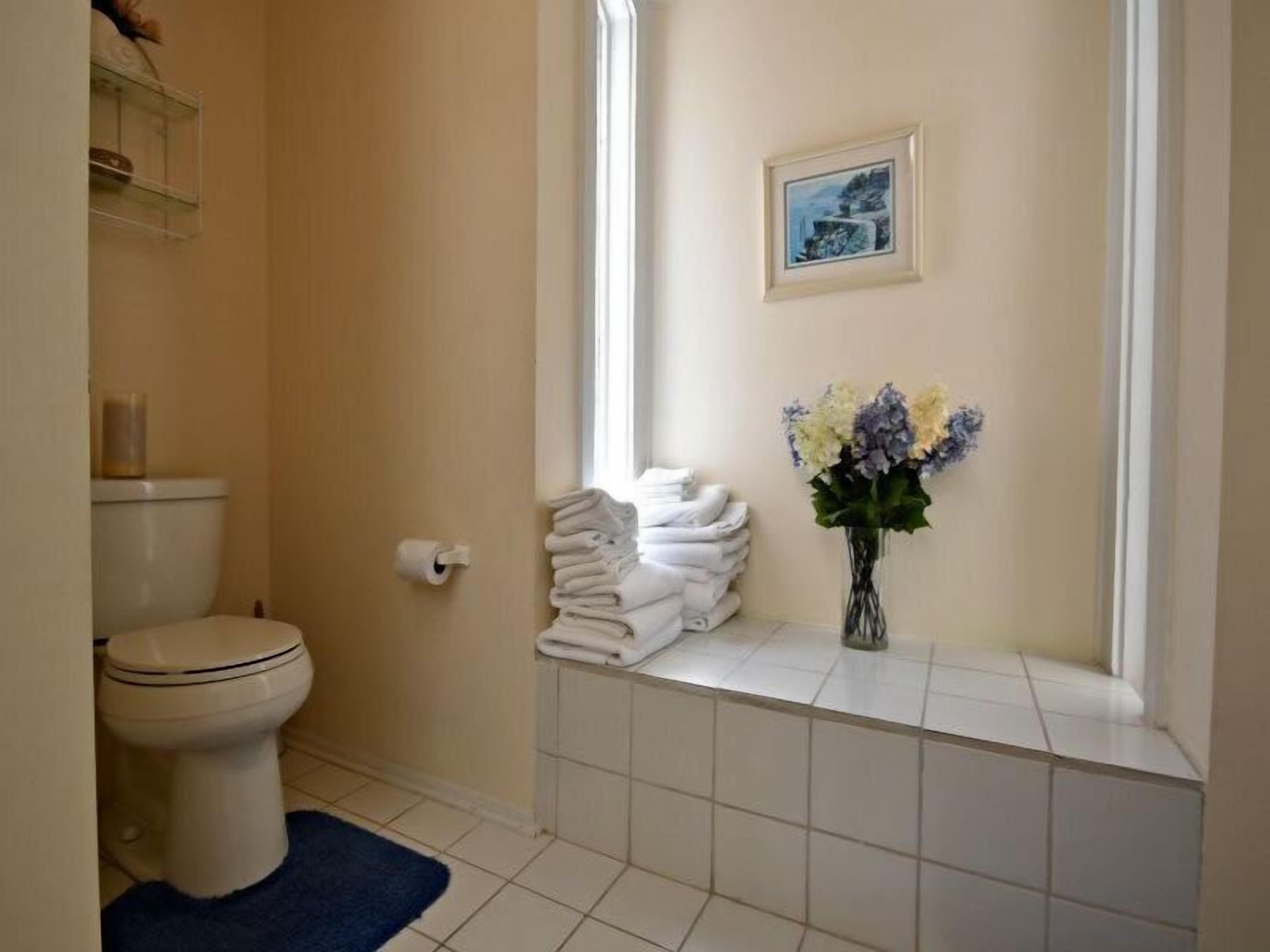 A bathroom with a toilet, a roll of toilet paper, a stack of towels, and a vase with flowers.