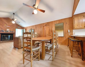 Un intérieur en bois comprenant une table à manger, des chaises, un ventilateur de plafond et une cheminée.