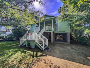 A two-story house with a front porch, a staircase, and a sign indicating beach vacation rentals.