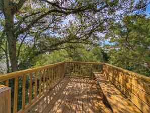 Une terrasse en bois, dotée de rampes de protection, entourée d’arbres.