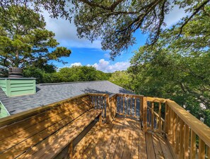 A wooden deck with a railing, surrounded by trees and a clear sky.