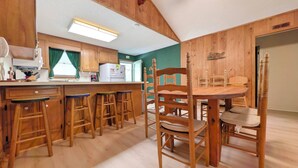 A kitchen with wooden cabinets, a dining table with chairs, and a bar area with stools. - Longs for the Sea - North Litchfield Beach (Pawleys Island)