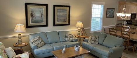A living room with a sofa, coffee table, and lamps. There is a dining area with a table and chairs.