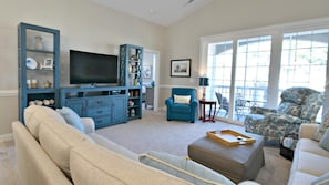 A living room with a large flat-screen TV, a blue armchair, a beige sofa, and a patterned armchair.