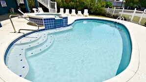Una piscina con borde de baldosas, sillas de descanso y una zona pequeña de hidromasaje.