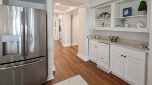 Una cocina moderna con armarios blancos, un refrigerador de acero inoxidable y una encimera con un bol y una cesta.