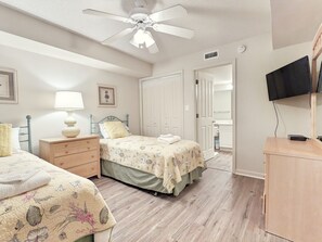 Un dormitorio con dos camas, ventilador de techo, televisor y cómoda de madera.