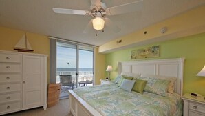 A bedroom with a large bed, a ceiling fan, a nightstand, a dresser, and a view of the ocean through a sliding glass door. - Oceanfront Condo - Litchfield by the Sea - Community Pool & Hot Tub (Pawleys Island)