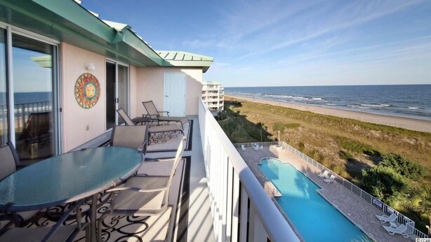 A balcony with a glass table and chairs, overlooking a beach and a pool. - Oceanfront Condo - Litchfield by the Sea - Community Pool & Hot Tub (Pawleys Island)