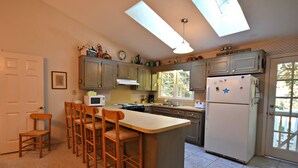 A kitchen with a central island, bar stools, a microwave, a stove, and a refrigerator. - Our Favorite Perch Second Row - North Litchfield Beach (Pawleys Island)