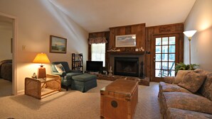 A cozy living room with a fireplace, a sofa, a loveseat, a coffee table, and a wicker side table with a lamp. - Our Favorite Perch Second Row - North Litchfield Beach (Pawleys Island)