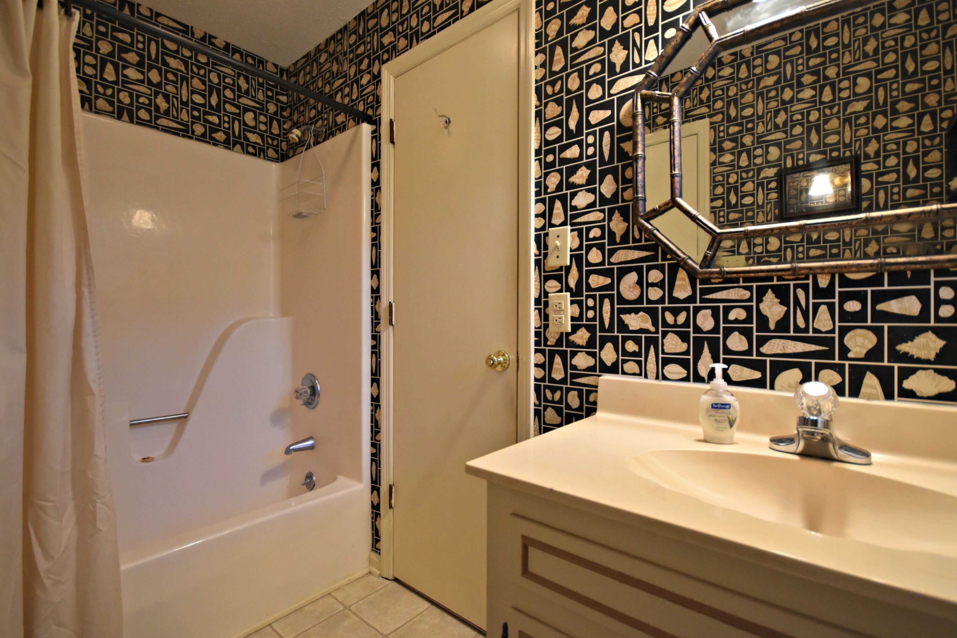 A bathroom with a bathtub, a sink with a mirror, and patterned tiles on the walls.