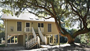 A two-story building with a staircase leading to a balcony, surrounded by trees. - Our Favorite Perch Second Row - North Litchfield Beach (Pawleys Island)