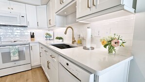 Een moderne keuken met witte kasten, een ingebouwde oven, een vaatwasser en een gootsteen met een gouden kraan.