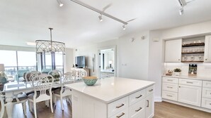 Een moderne keuken met witte kasten, een centraal eiland en een eethoek met witte stoelen en een tafel.