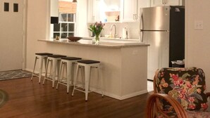 Una cocina con armarios blancos, un refrigerador de acero inoxidable y una zona de bar con taburetes.