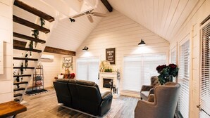 Un salon chaleureux avec une cheminée, un plancher en bois, un canapé en cuir noir et un fauteuil gris.