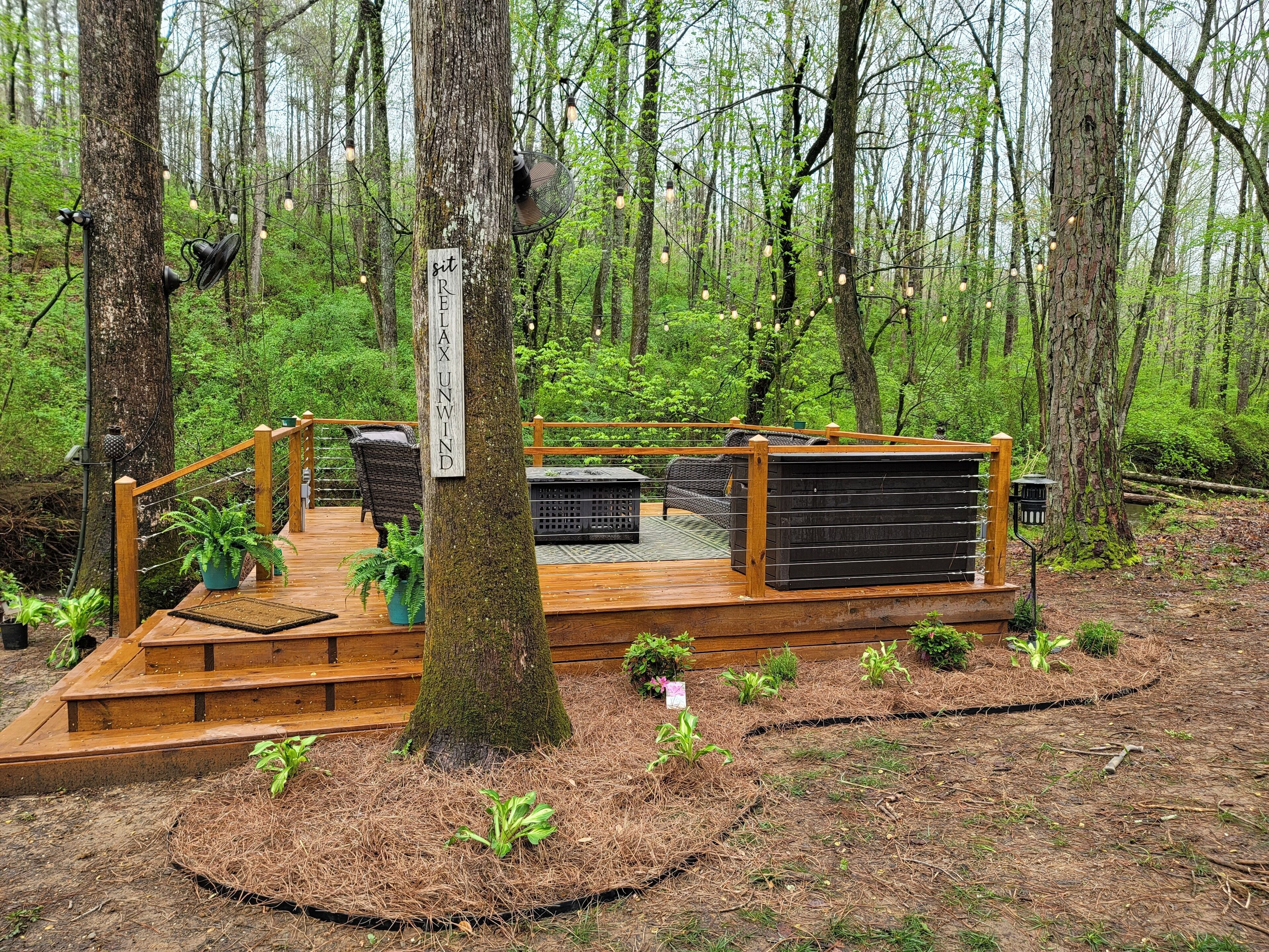 A wooden deck with a sign reading "sit REI TAX UNWIND" surrounded by a forest.