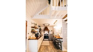Une cuisine étroite avec un plancher en bois, des meubles blancs et un îlot central.