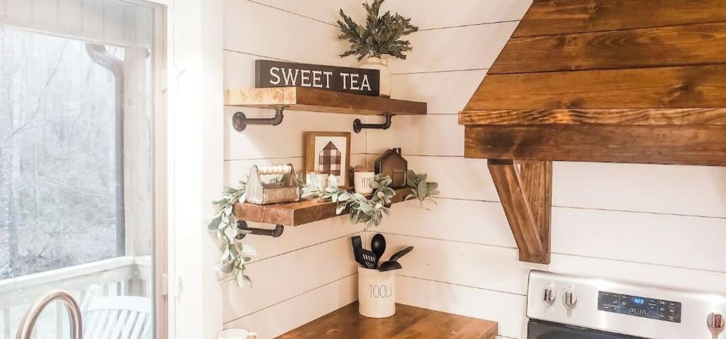 Una cocina con estantes de madera, un cartel que dice 'SWEET TEA' y un electrodoméstico blanco sobre la encimera.