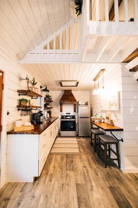 Una cocina estrecha con suelo de madera, armarios blancos y una isla central.