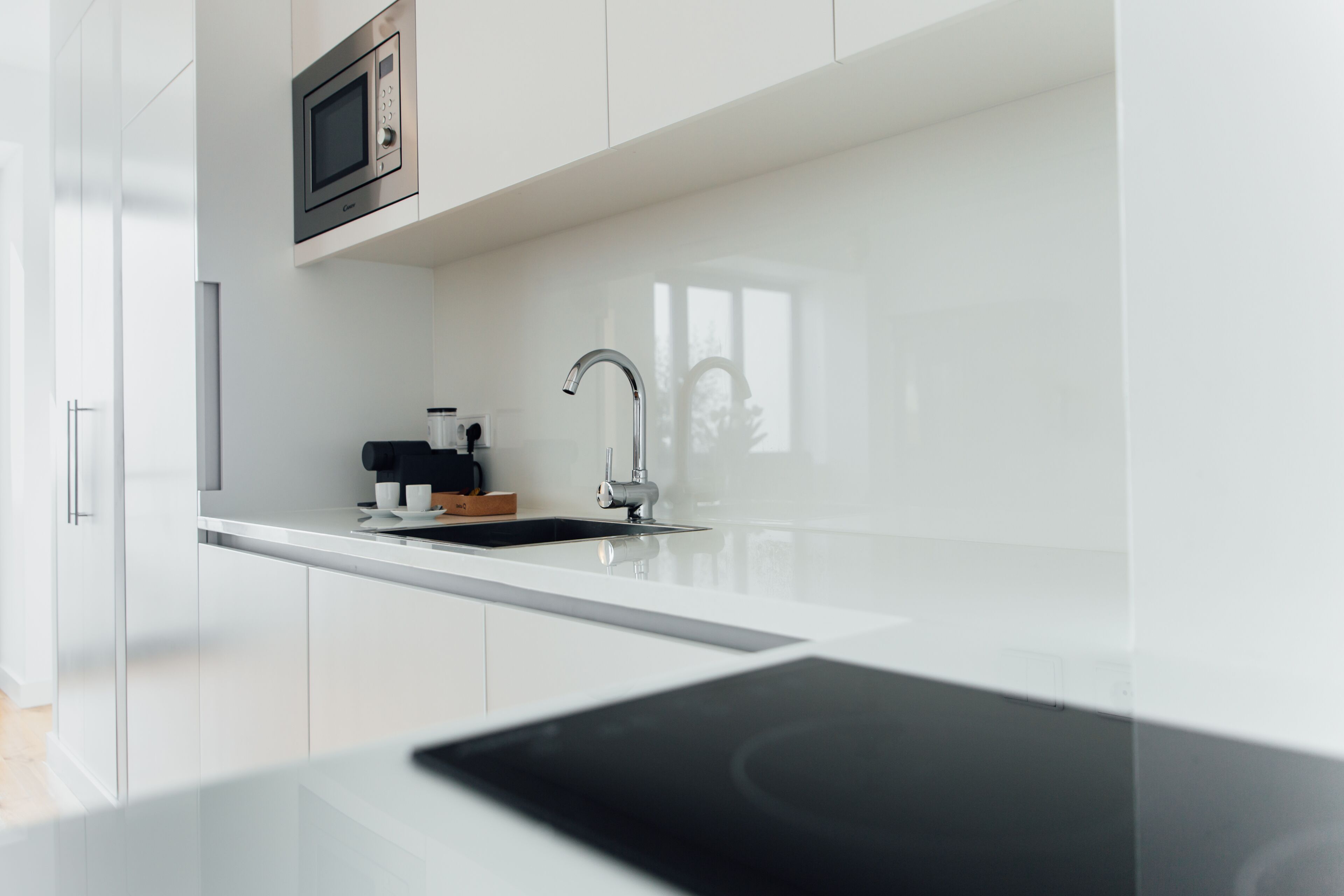 Una cocina moderna con armarios blancos, microondas de acero inoxidable, cafetera y encimera negra.