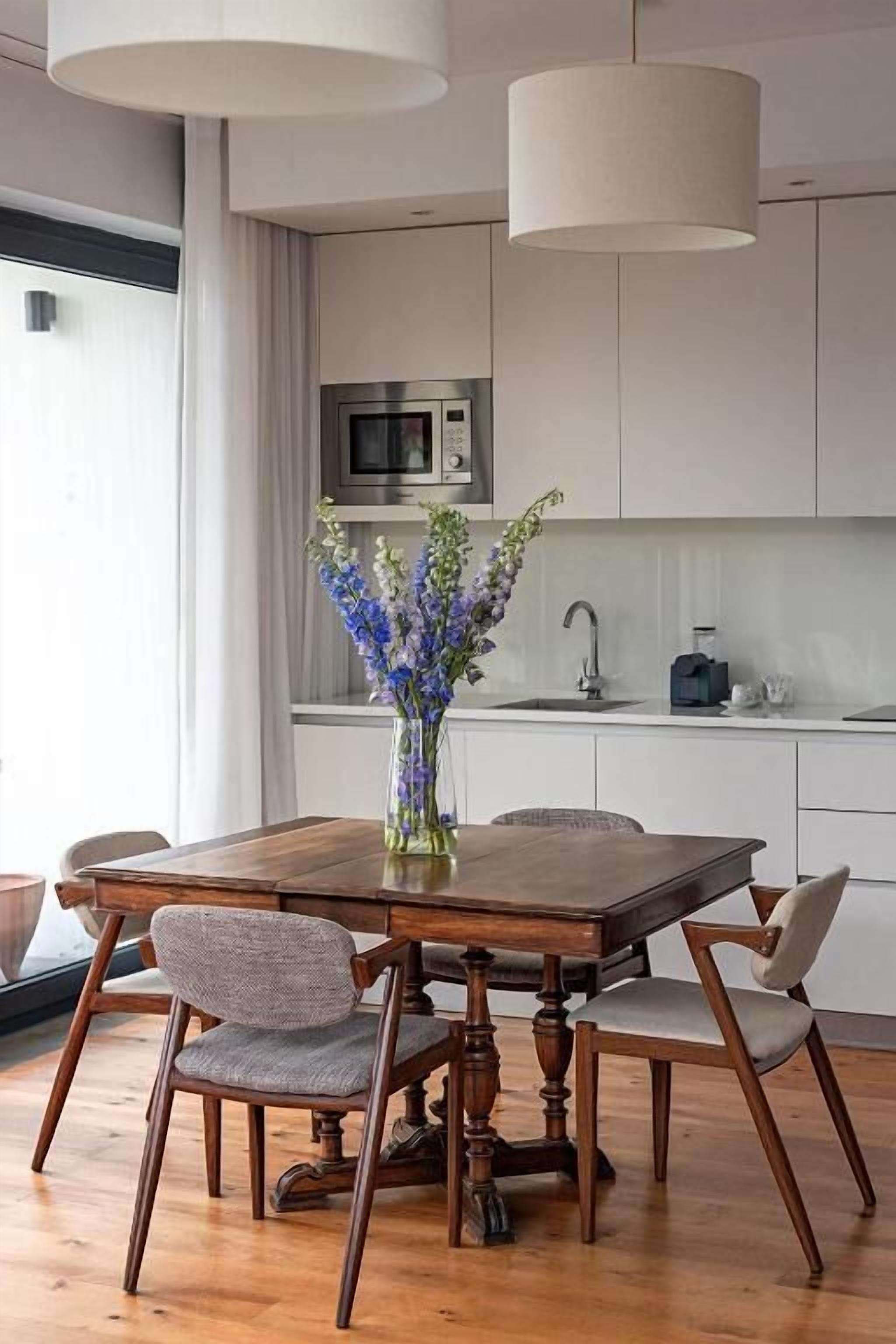 A modern kitchen with a wooden dining table, chairs, and a vase of flowers.