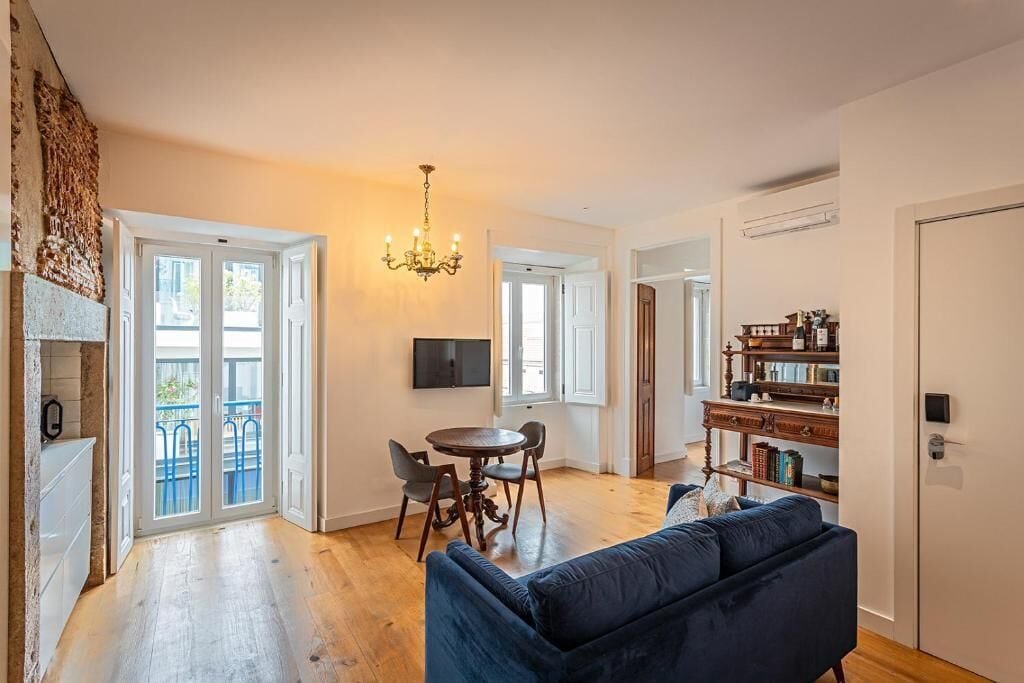 Ein geräumiger Wohnbereich mit blauem Sofa, einem Esstisch mit Stühlen, einer Chandelierleuchtre und einem Bücherregal.