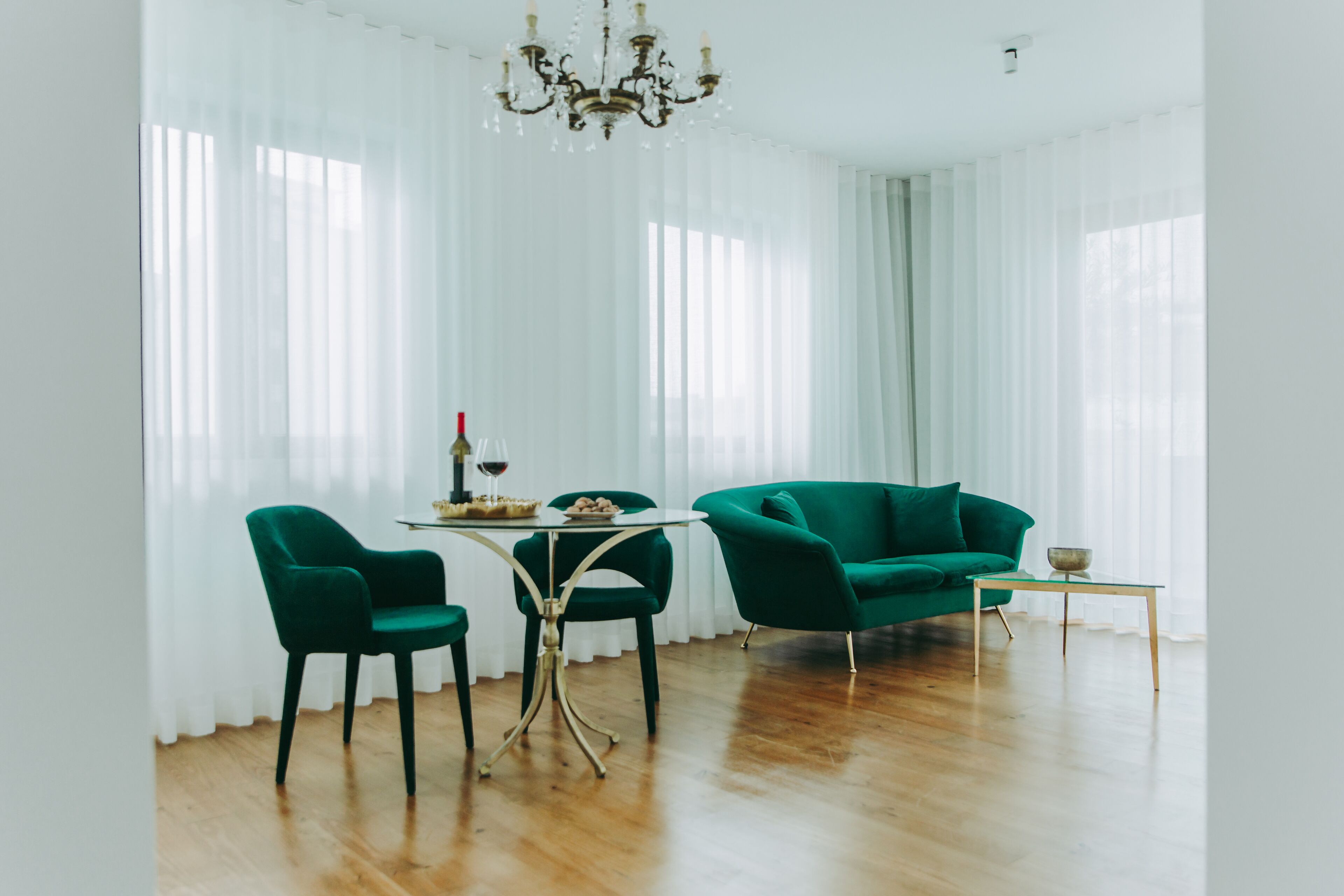 A room with a green sofa, two green chairs, a small table, and a chandelier.