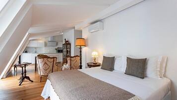 Ein Schlafzimmer mit einem großen Bett, einem Schreibtisch und einem Stuhl. Im Hintergrund ist eine Küche zu sehen.