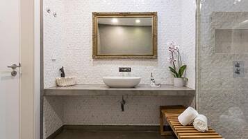A bathroom with a white sink, a gold-framed mirror, a wooden bench with towels, and a potted orchid.