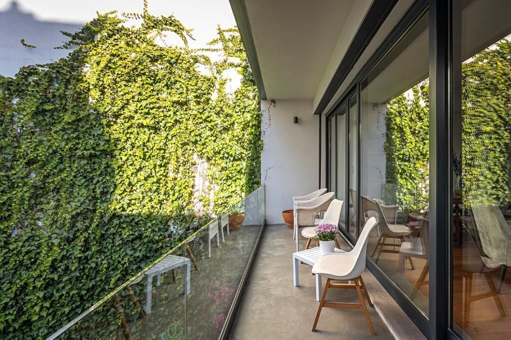 A balcony with a glass railing, white chairs, and a potted plant.