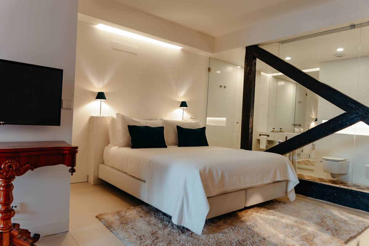 A modern bedroom with a large bed, bedside lamps, a flat-screen TV, and a wooden nightstand.