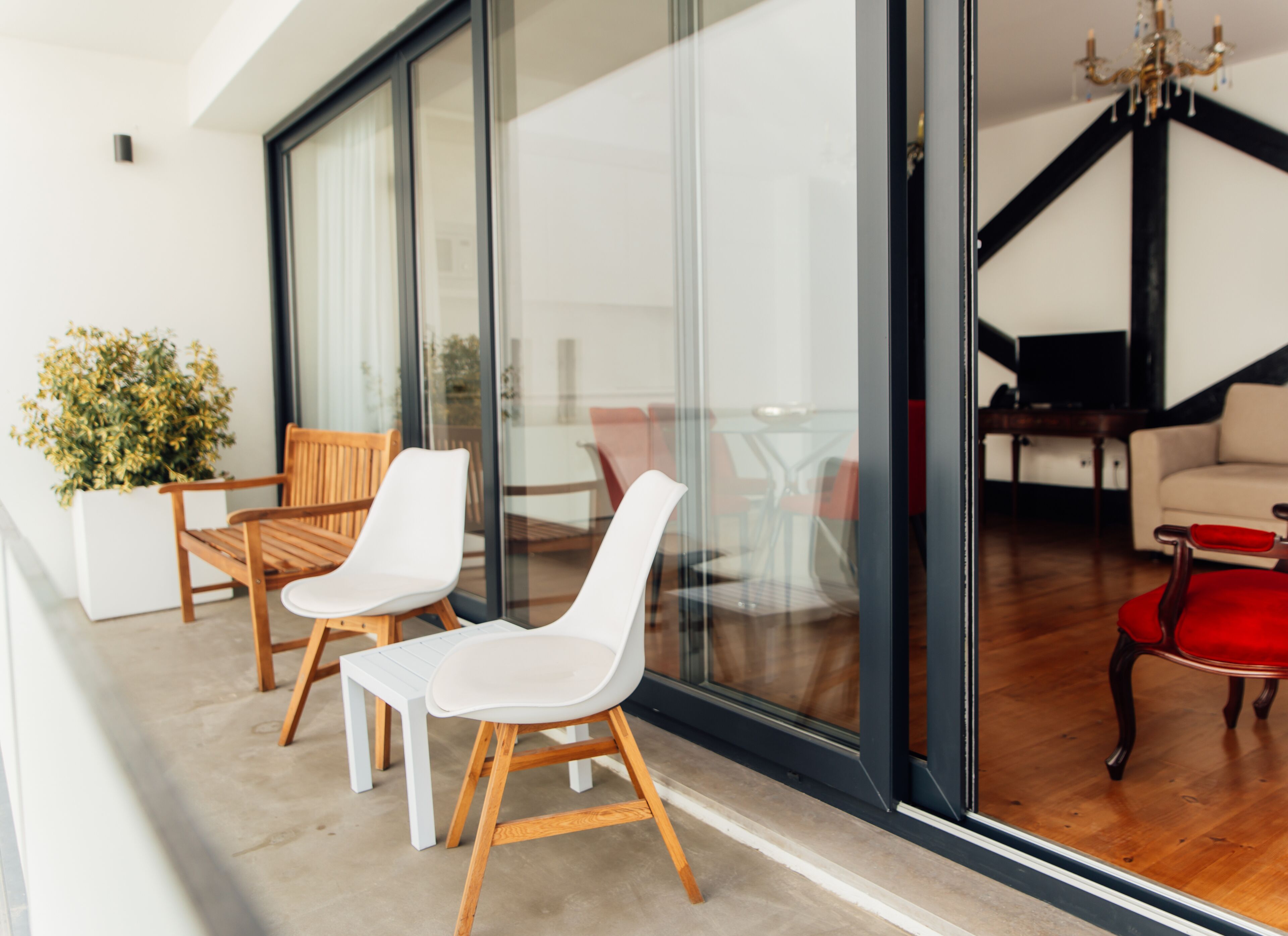 A modern interior with a glass sliding door leading to a dining area with wooden and white chairs, a potted plant, and a chandelier.