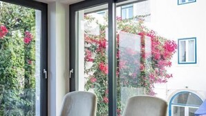 A room with two armchairs, large windows, and a view of a building with pink flowers outside. - 54 São Paulo – Exclusive Apartment Hotel (Lisbon)
