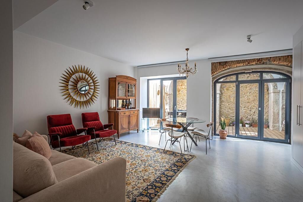 Uma sala de estar ampla com um sofá bege, cadeiras vermelhas, um armário de madeira e um lustre.