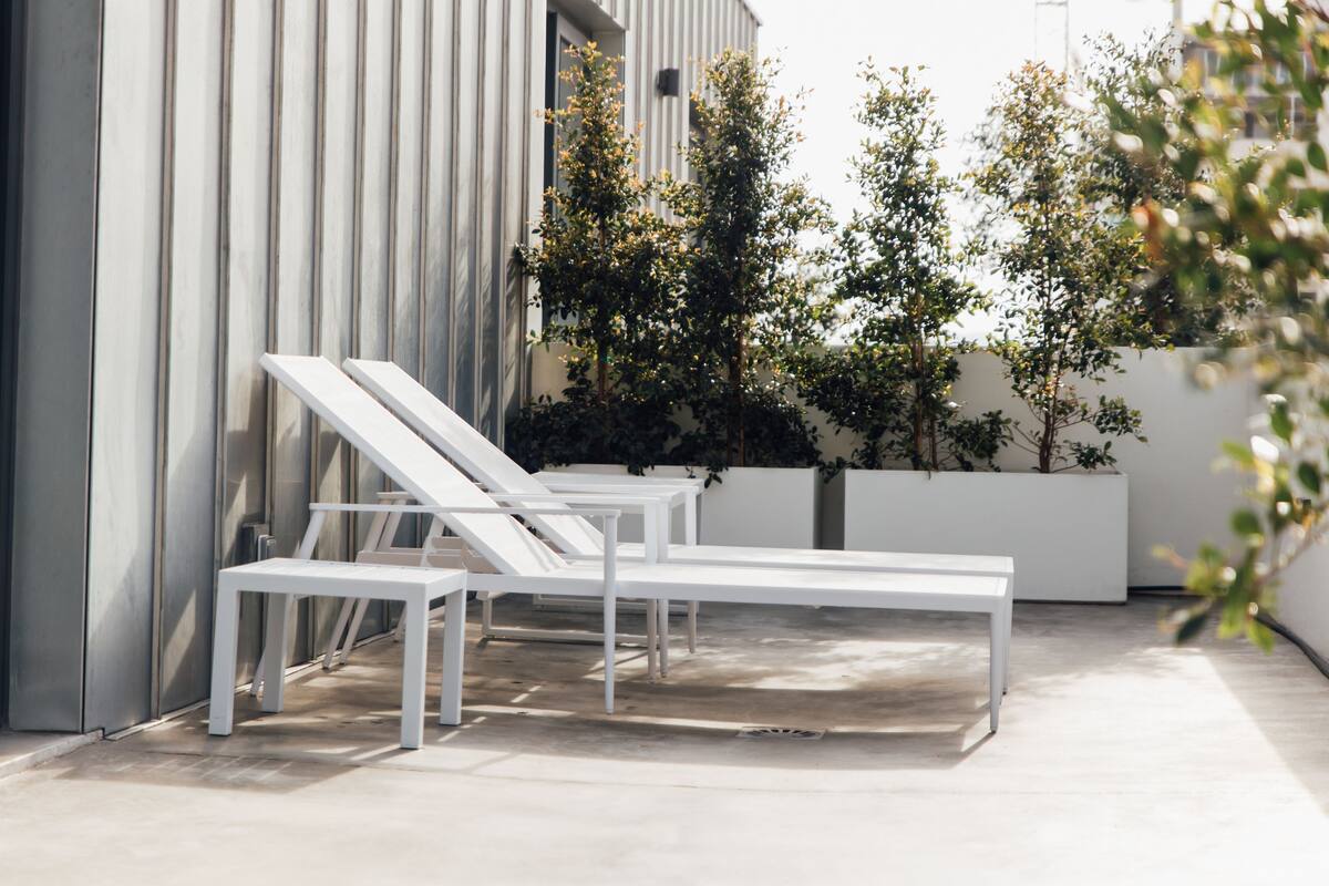 A modern outdoor lounge area with white lounge chairs and a concrete floor.