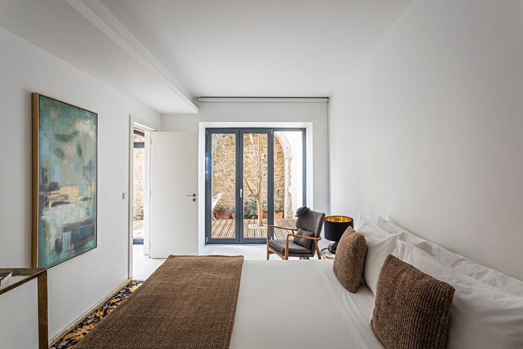 Una camera da letto con un letto grande, una sedia, una lampada e vista su uno spazio esterno tramite una porta scorrevole.