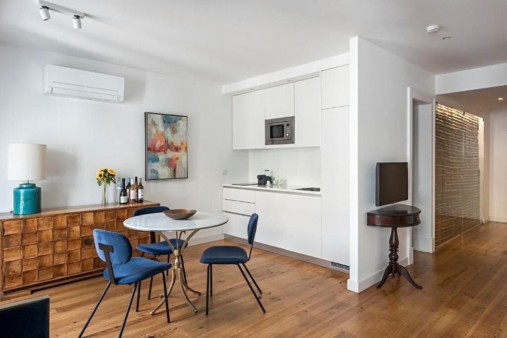 A modern kitchen with white cabinets, a microwave, and a dining area with blue chairs and a round table.